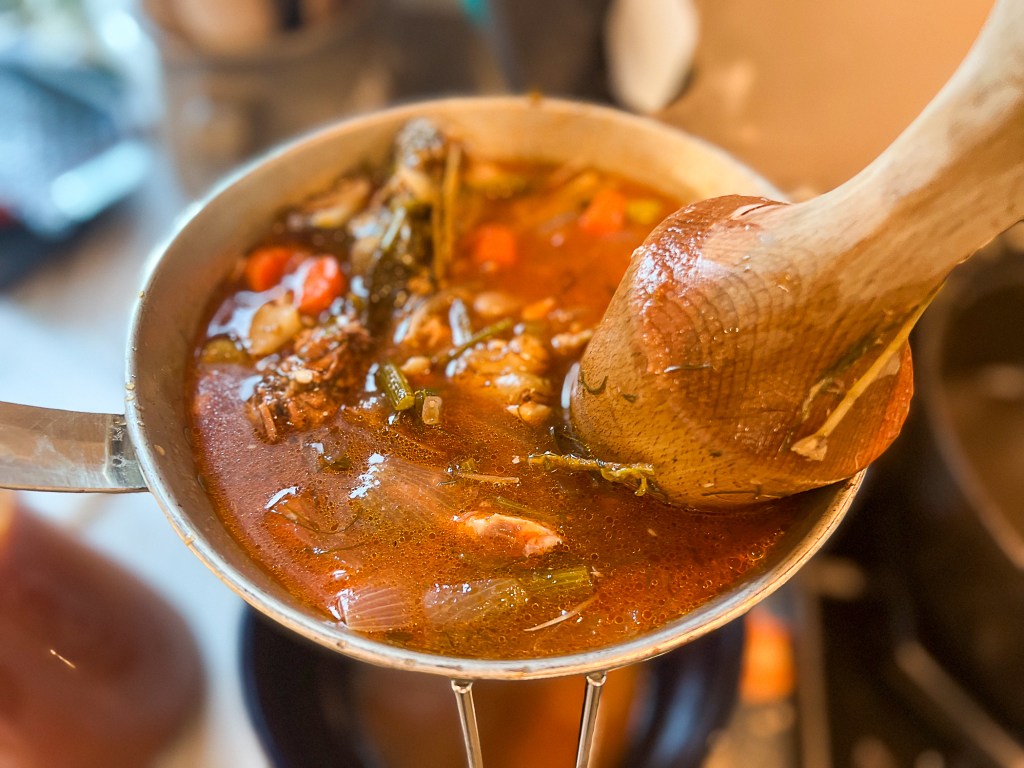 A close-up view of a pot of soup being stirred with a wooden spoon, featuring various vegetables and ingredients in a rich broth.